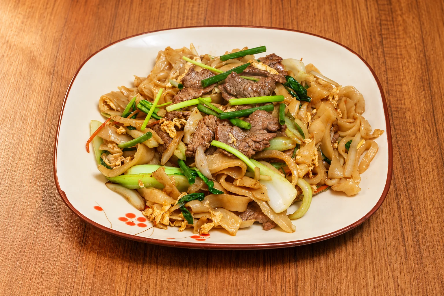 Knife-cut noodles with spicy beef on a brown-rimmed plate, wooden table