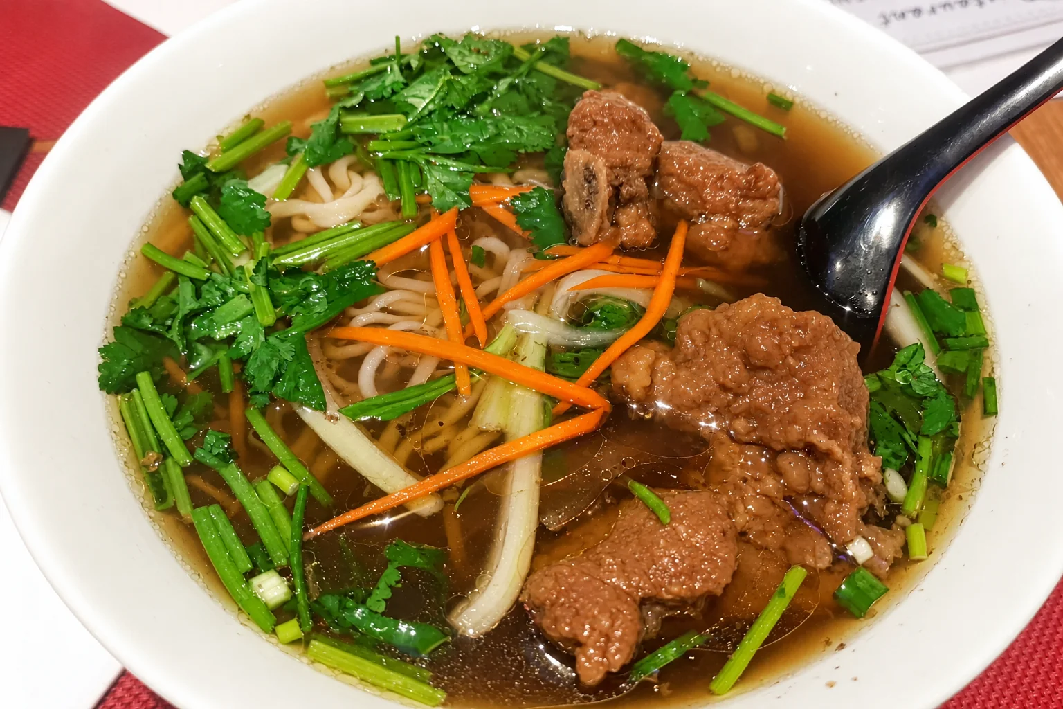 Noodle soup in a white bowl, black spoon