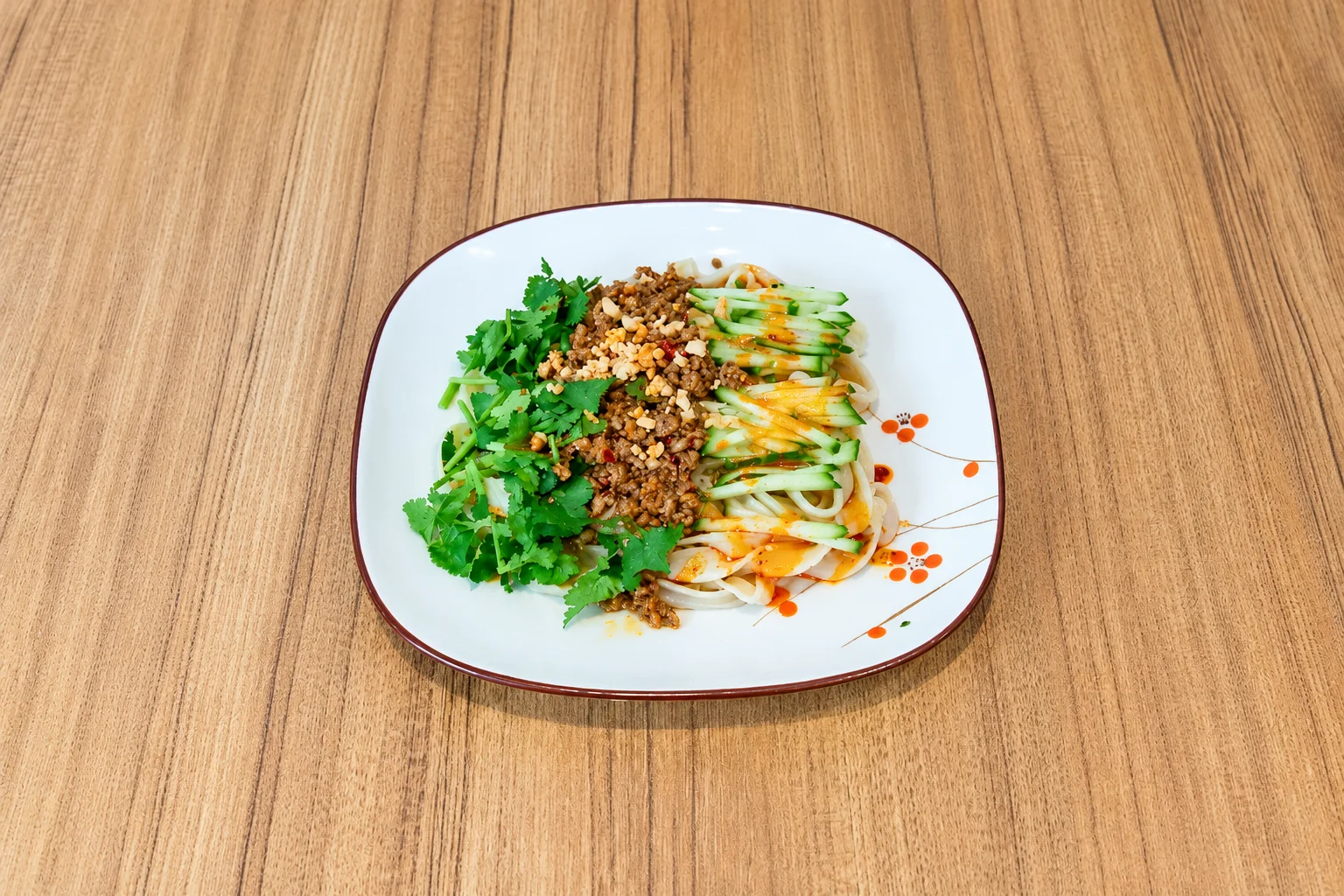 Cold noodles with minced pork on a brown-rimmed plate, wooden table