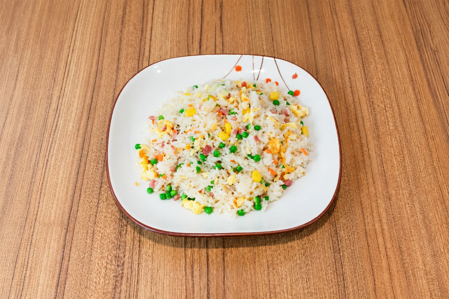 Cantonese fried rice on a brown-rimmed plate, wooden table