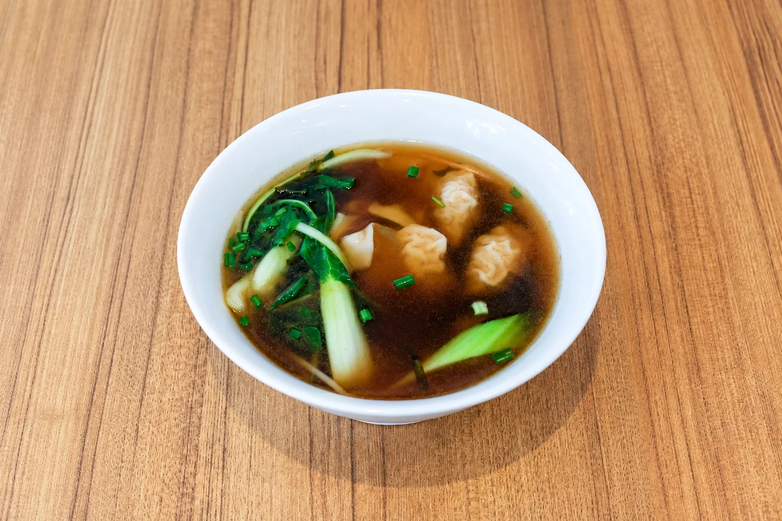 Chinese dumpling soup in a white bowl, wooden table